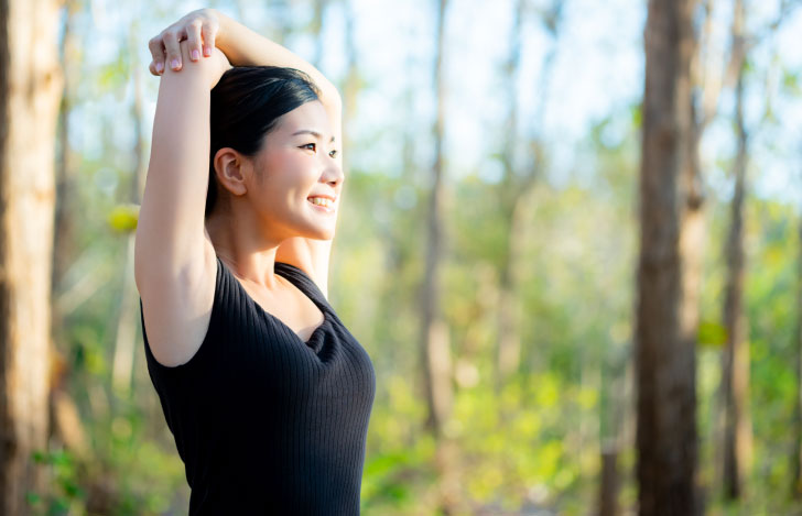 手で反対側の肘を掴んで伸びをする笑顔の女性