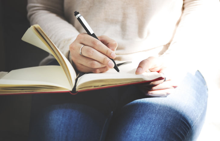 膝の上に手帳を広げて日記を書く女性の手元