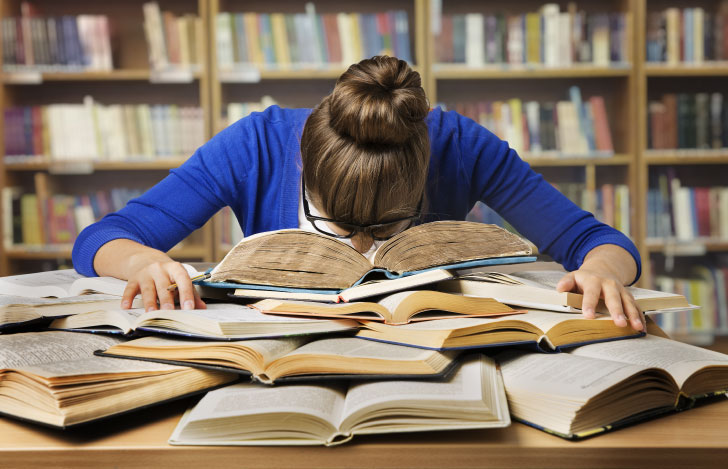 山積みの本の上に覆いかぶさるように顔を埋める女性