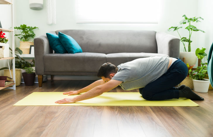 自室のヨガマットの上でチャイルドポーズをとる男性