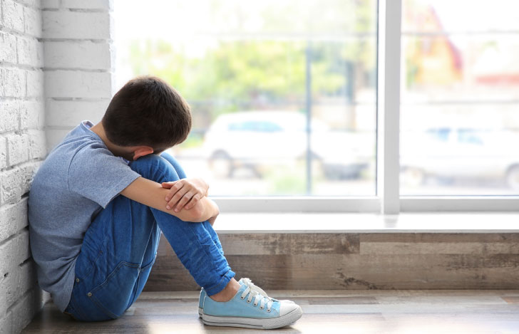 窓辺で膝を抱えてうなだれる少年