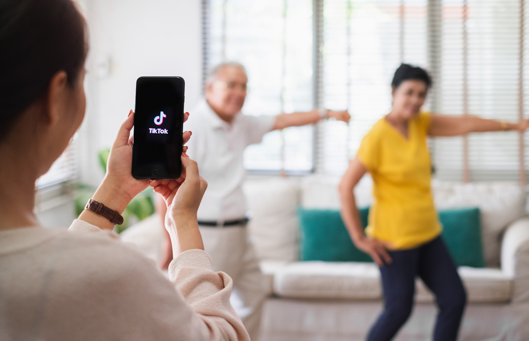 TikTokのロゴが入った黒い携帯で、2人の踊っている男女を撮影する女性