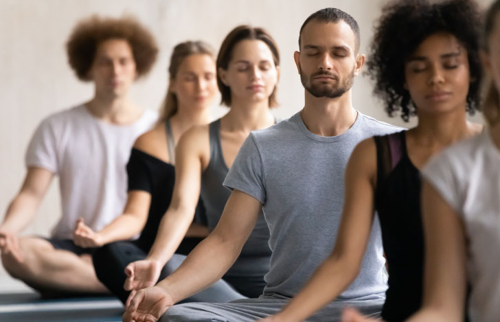 目を閉じて瞑想を行う複数の男女