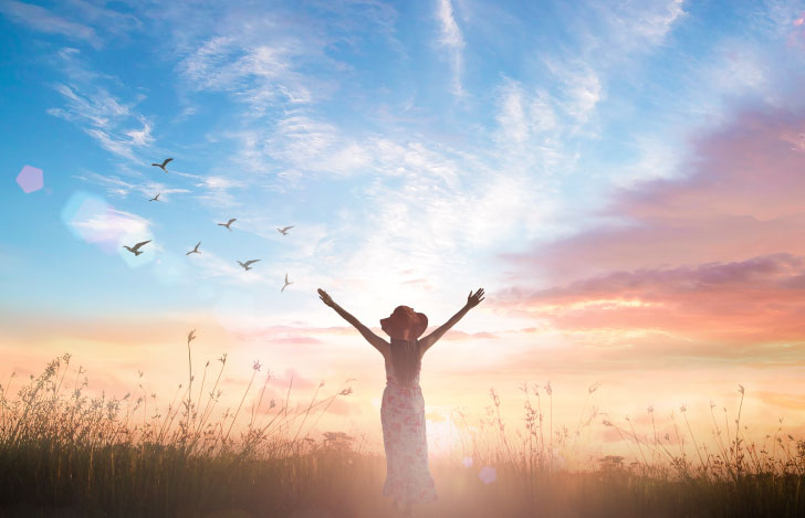 空に向かって両手を広げる女性の後ろ姿