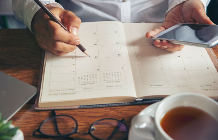 スマホを片手に鉛筆で手帳に書き込む人の手元