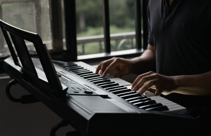 薄暗い部屋でピアノを弾く少年の手元