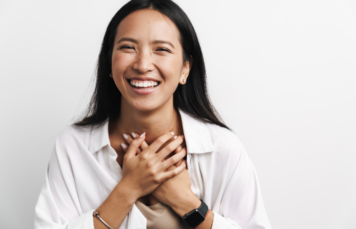 白いシャツを着て胸に手を当てる笑顔の女性