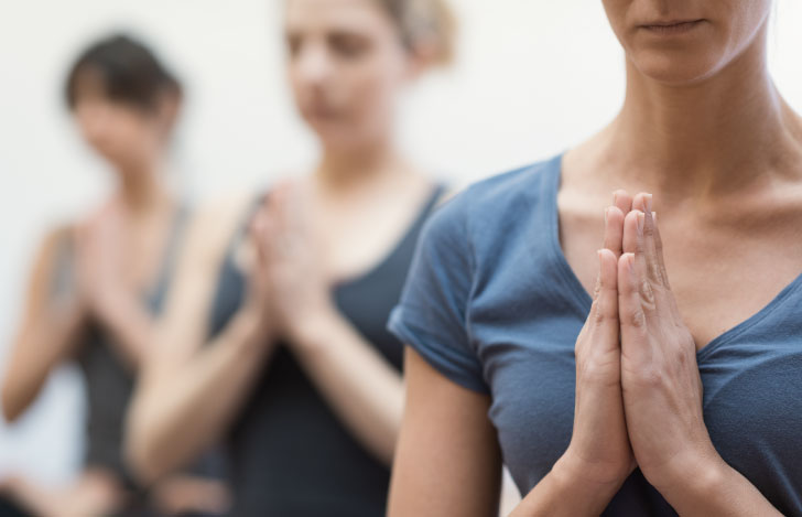 ヨガのクラスで目を閉じて合掌する人々