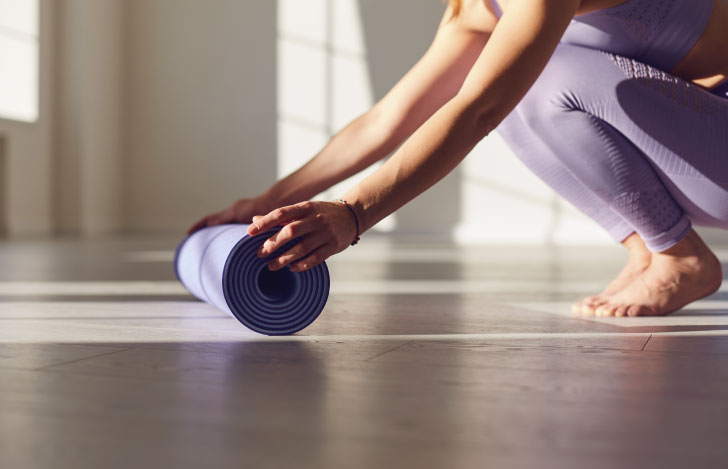 床の上のヨガマットを丸めている女性の手元