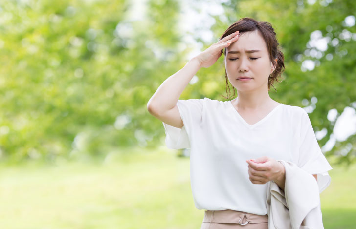 屋外でめまいを覚え額に手を当てる女性