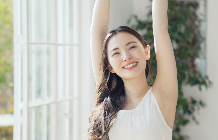 窓辺で伸びをする笑顔の女性