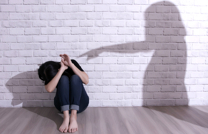 壁の前でうずくまる女性に指差す人の影