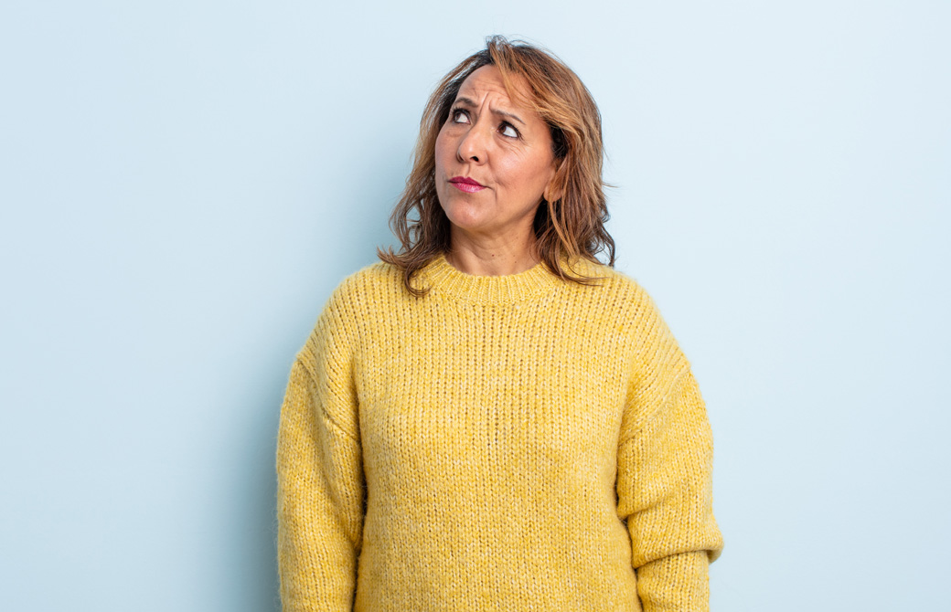 黄色のセーターを着て、しかめっ面で斜め上を見る金髪の女性