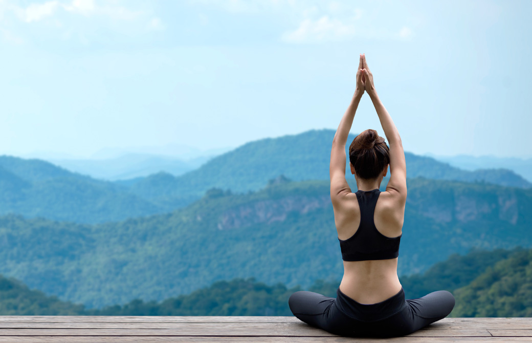 あぐらで合わせた両手を掲げるウェアを着た女性