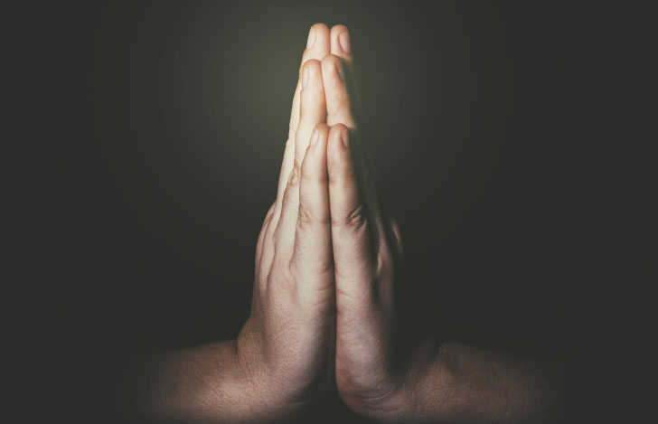 闇の中で薄明かりを手元に受ける合掌の手