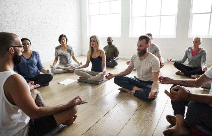 老若男女さまざまな人が指導者のもとでヨガを練習する様子