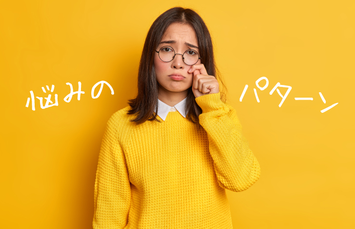 困った表情を浮かべ手を目元に添える黄色いセーターの女性