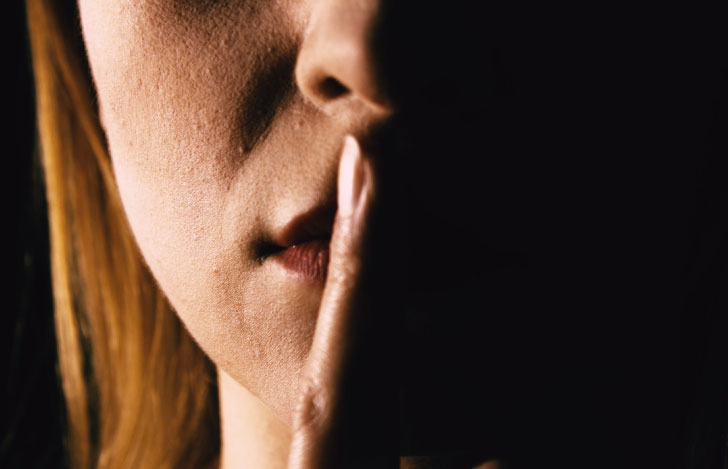 薄暗がりで口元に人差し指を当てる女性の口元