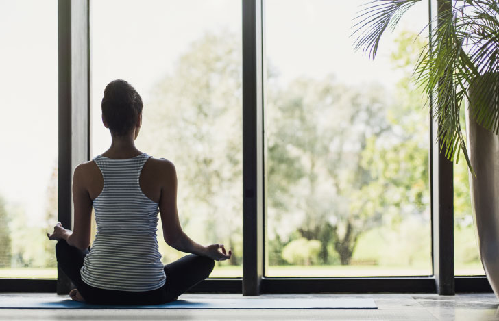 大きな窓に向かって瞑想する女性の後ろ姿