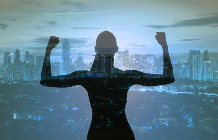 ビルが立ち並ぶ都会の風景に向かってパワフルなポーズをとる女性のシルエット