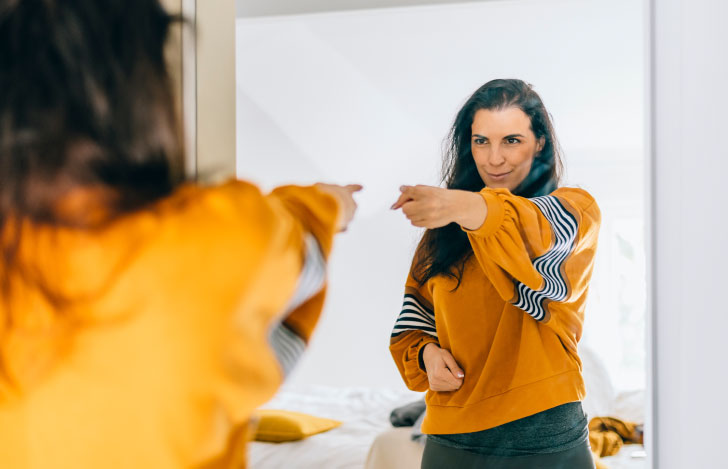 鏡の中の自分に向かって指をさす黄色い服を着た女性