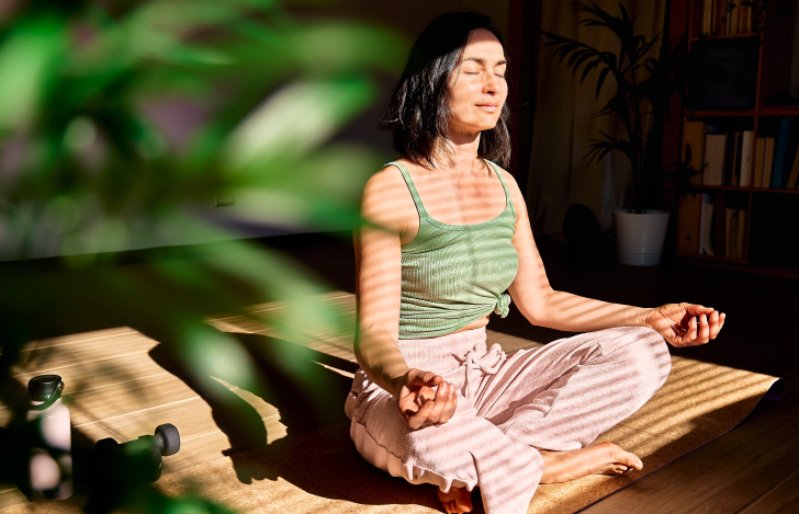 室内で安楽座で座りながらくつろいだ様子で瞑想をする女性
