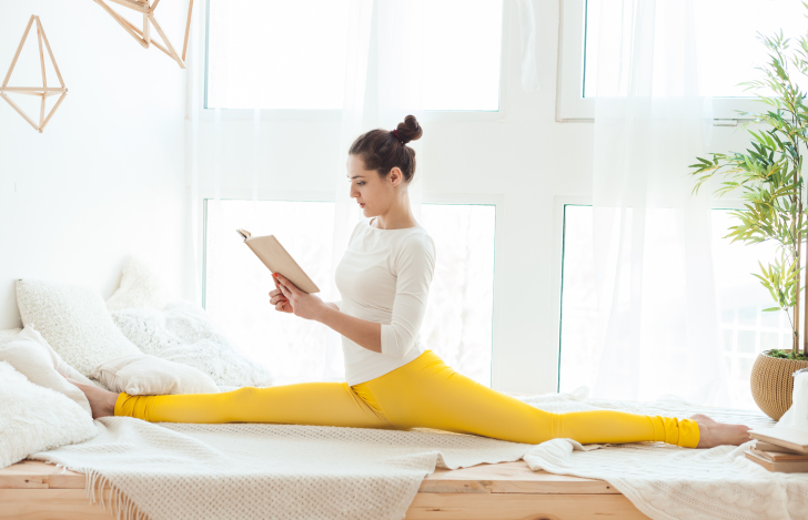 前後開脚をしながら窓辺で本を読む女性