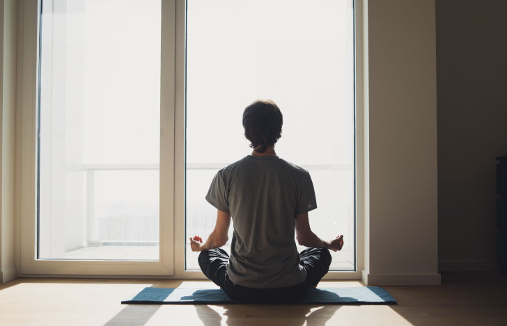 窓に向かって座り、瞑想する女性の後ろ姿