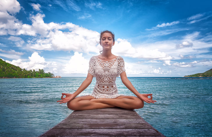 海と青空を背景に安楽座で座って瞑想する女性