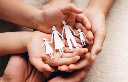 手のひらの上で紙でできた家族が手をつないでいる様子