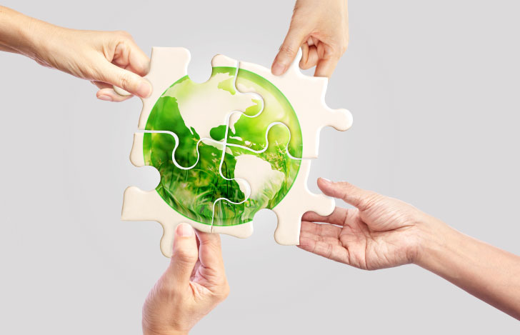 地球が描かれた4ピーズのパズルを組み合わせる人々の手元