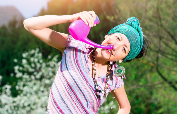 ピンク色のネティポットで鼻うがいを行う女性