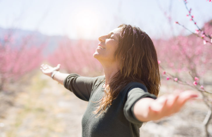 春の自然の中で両手を広げて空を仰ぐ女性