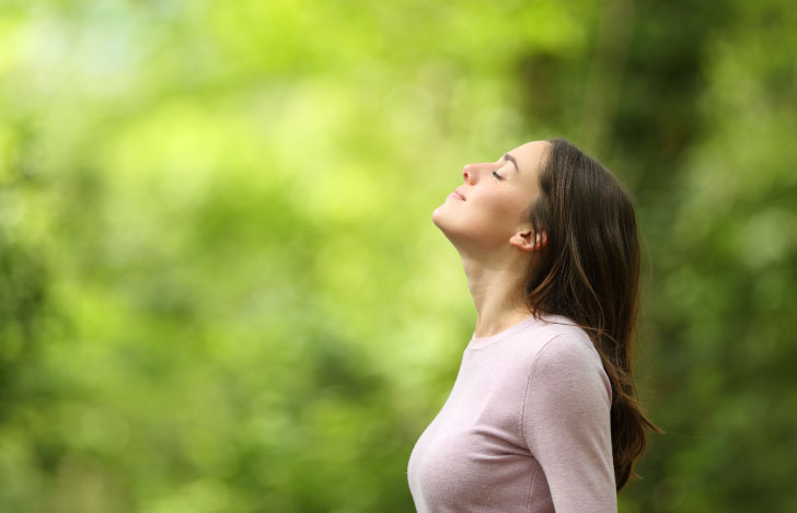 新緑の中で上を見上げて深呼吸する女性