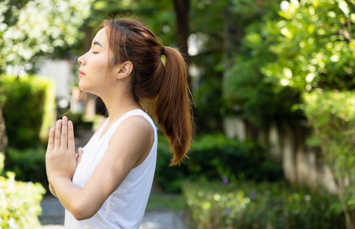自然の中で目を閉じ合掌する女性