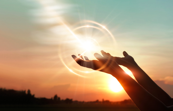 夕日が沈む空に向かって両手を伸ばす人の手元