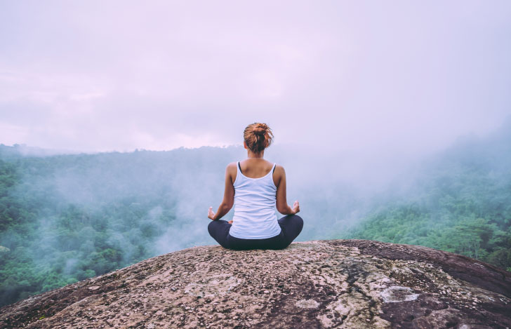 丘から見える森を見下ろしながら瞑想する女性の背中
