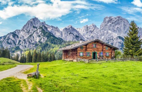 アルプスの山々と緑の草の上に立つ茶色い小屋