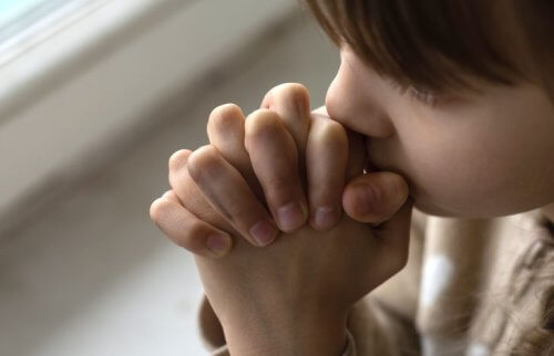 手を組んで口元に当てて願う女性