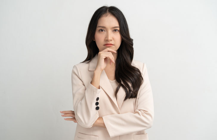 腕を組み手を顎に当てる白いジャケットを着た女性