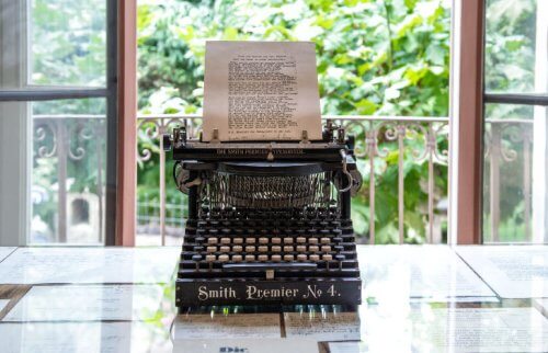 窓際に置かれたタイプライターとたくさんの文字が印字された紙