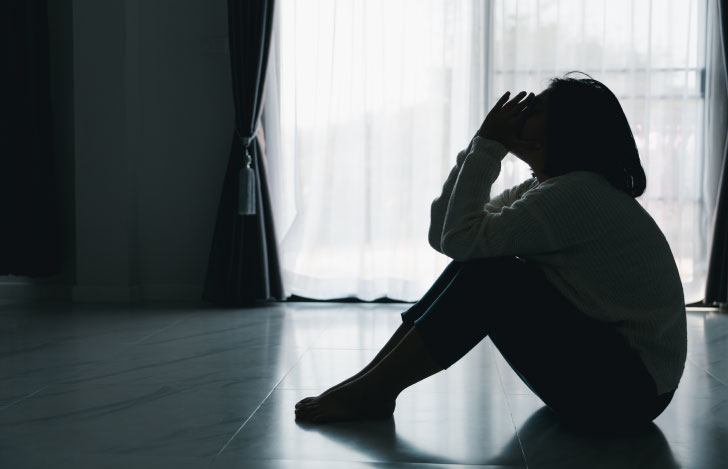 暗い室内でうずくまって座る女性のシルエット