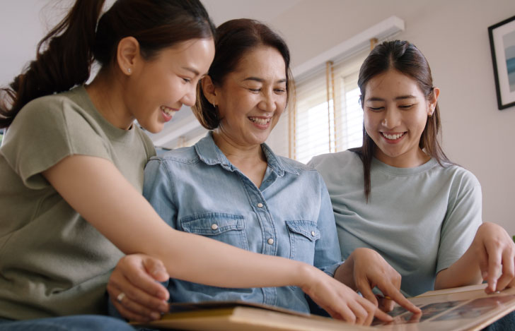 年配の女性と共にアルバムを絵がをで眺める2人の若い娘