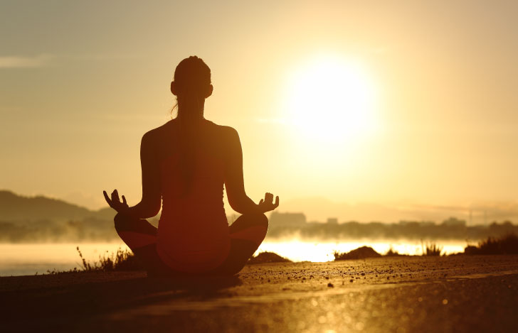 夕日に向かって安楽座で座る女性のシルエット