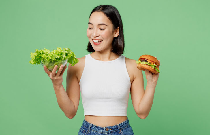 明るい白い服を着た若い女性が持つハンバーガーと新鮮な緑のレタス