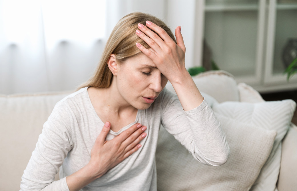 手で額と胸を押さえる、呼吸が苦しそうな女性