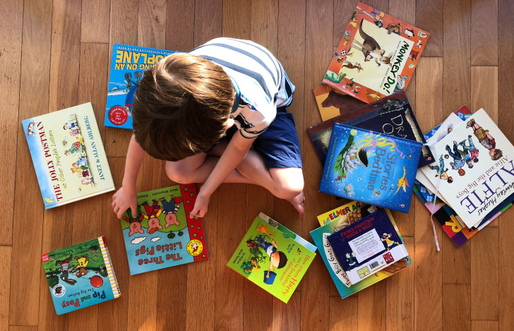 床に積み上げたたくさんの絵本の中に座る1人のこども