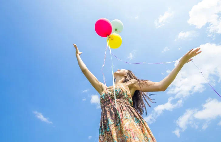 空に向かって両手を広げて風船を手放そうとしている女性