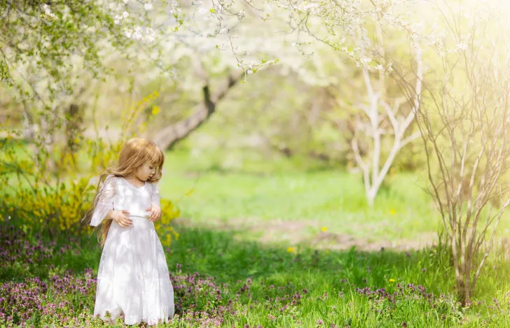 周囲を見ながら森の中を歩く白いワンピースを着た女の子