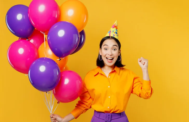 カラフルな風船を手に誕生日をイメージさせる三角帽を被った女性
